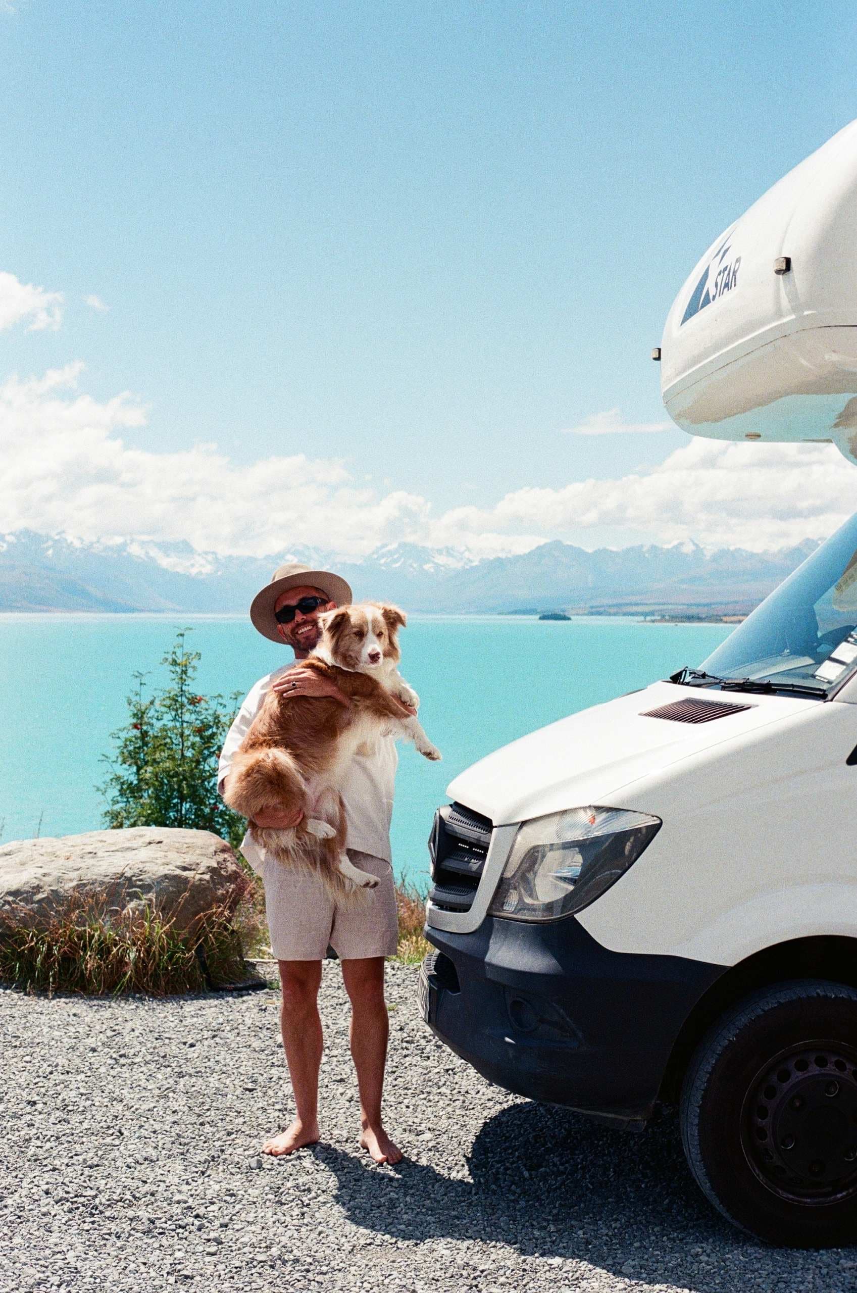 Man holding a dog standing next to Star RV motorhome hire with lake behind