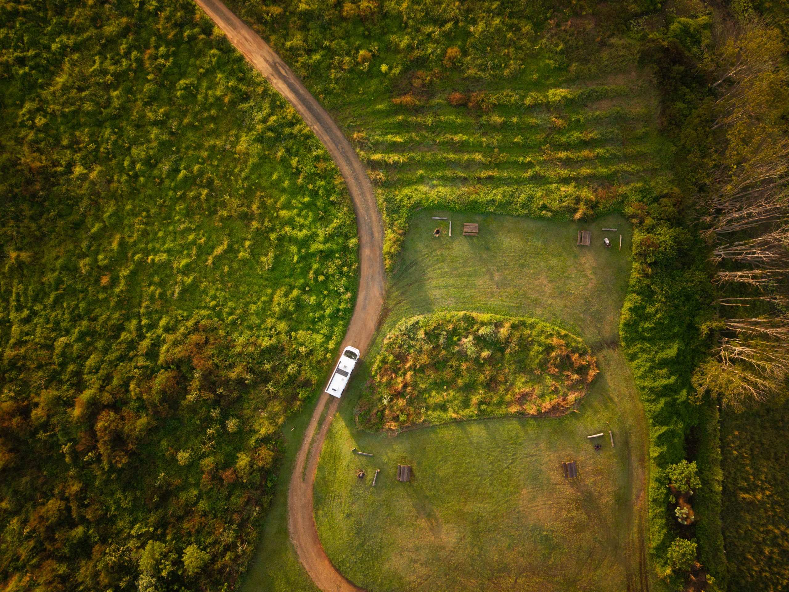 Polaris 2-berth motorhome driving on unsealed road past park benches overhead shot