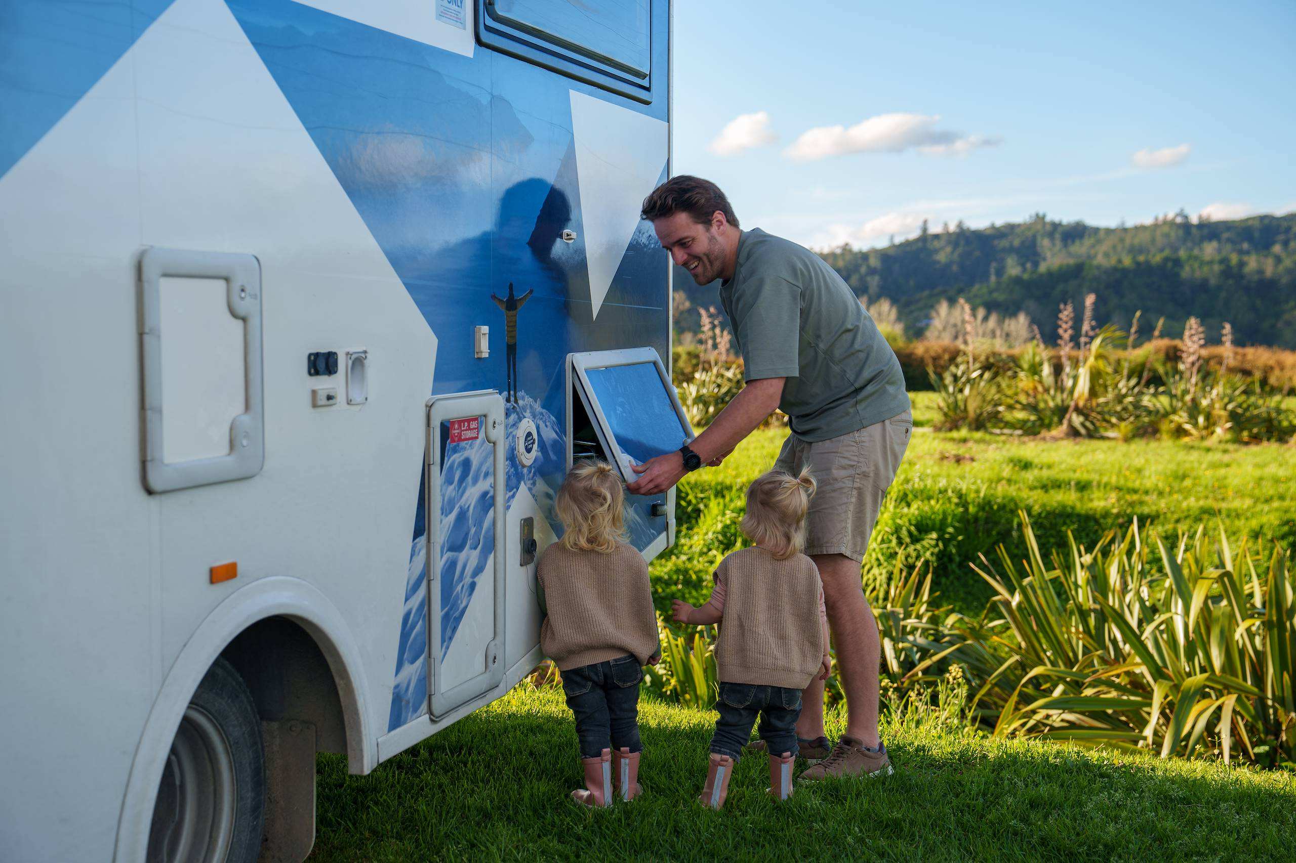 Father and two little twin girls opening exterior motorhome hatch for lpg gas