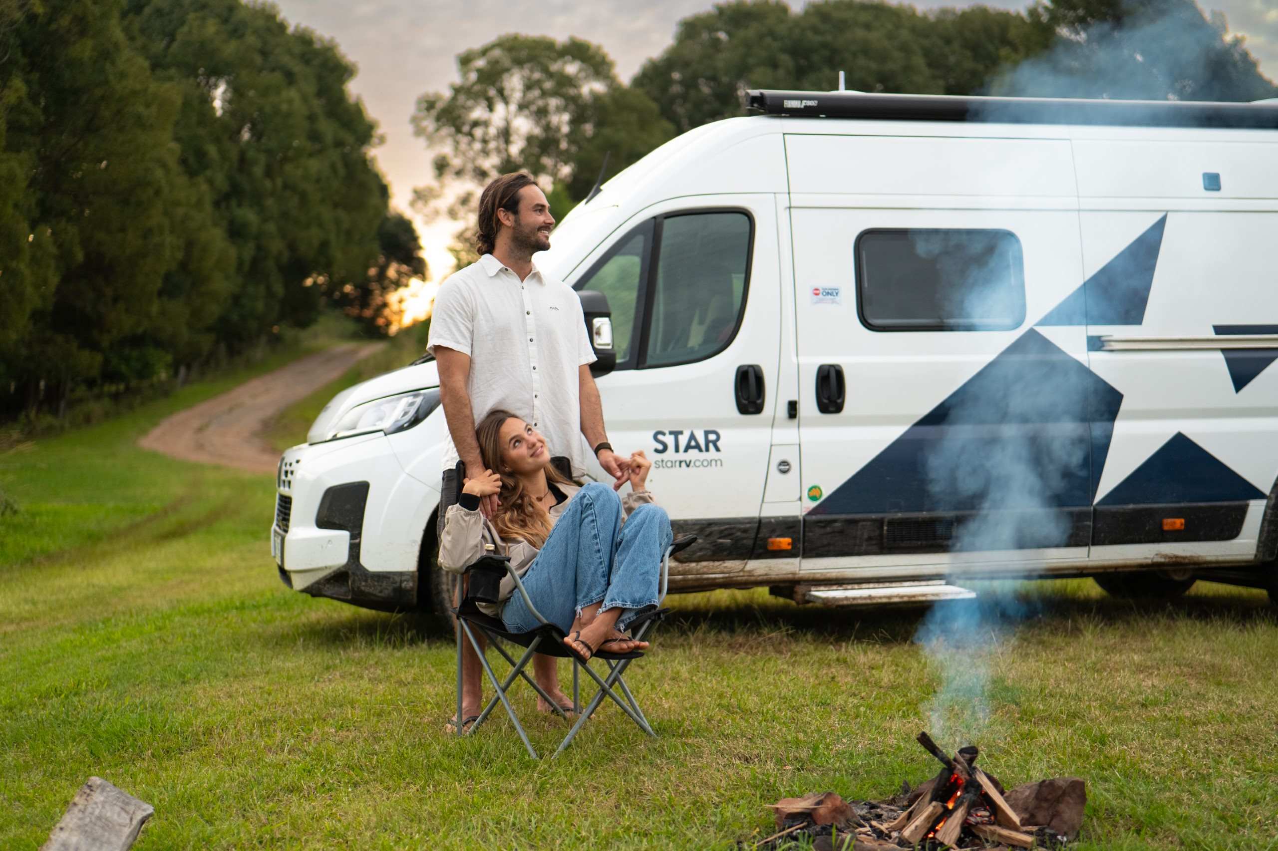 Couple sitting by smouldering fire outside motorhome in park