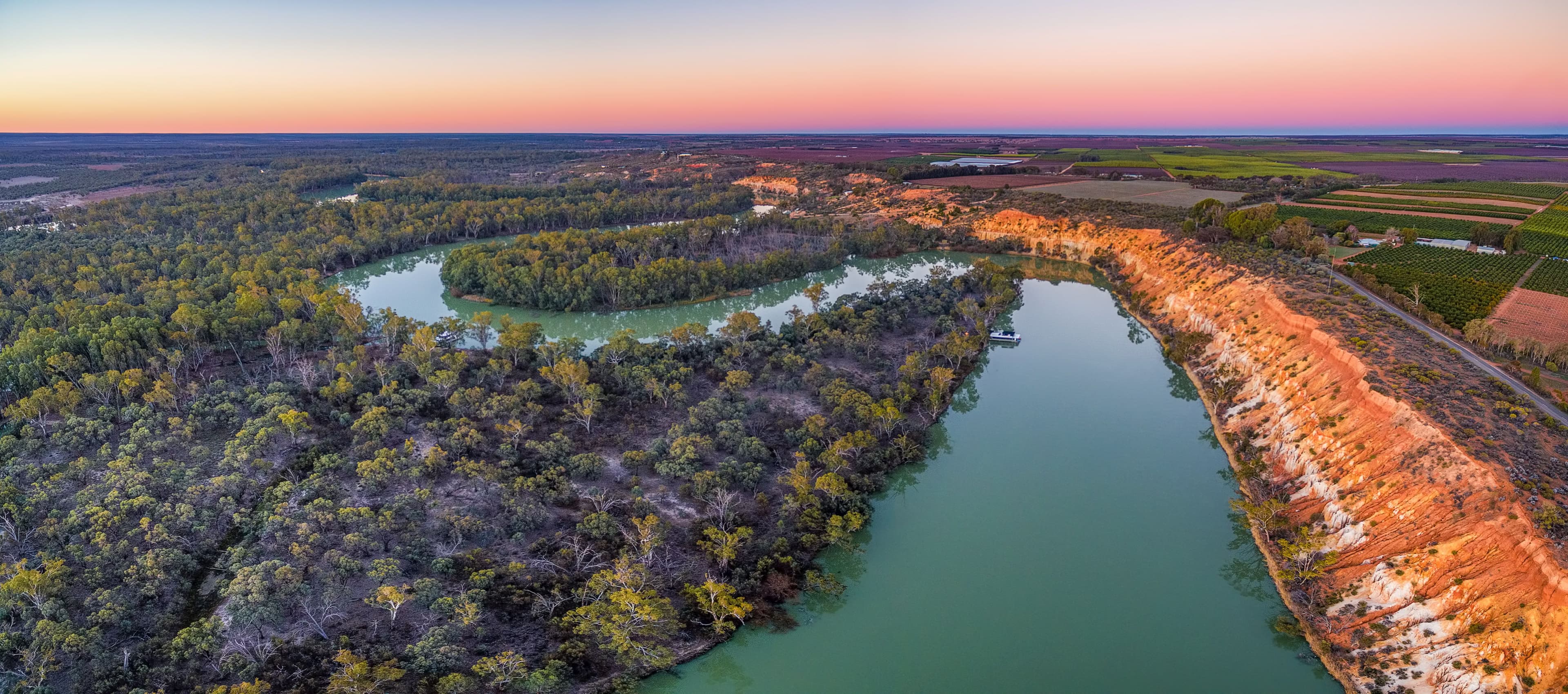 Aerial view of the Murray River at sunset, with a winding riverbed surrounded by lush greenery and red cliffs.