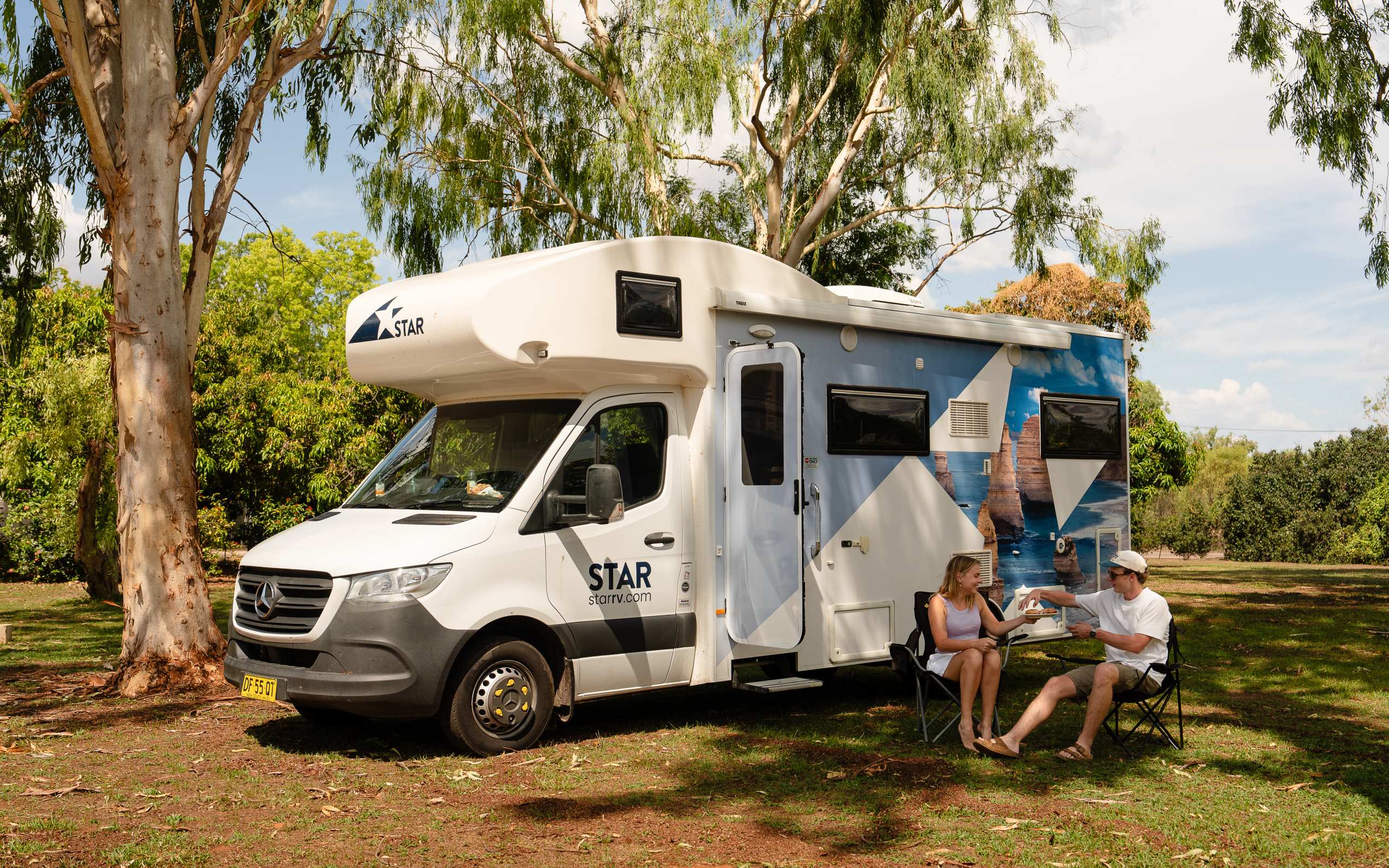 Couple sitting outside polaris-6 berth motorhome enjoying snacks