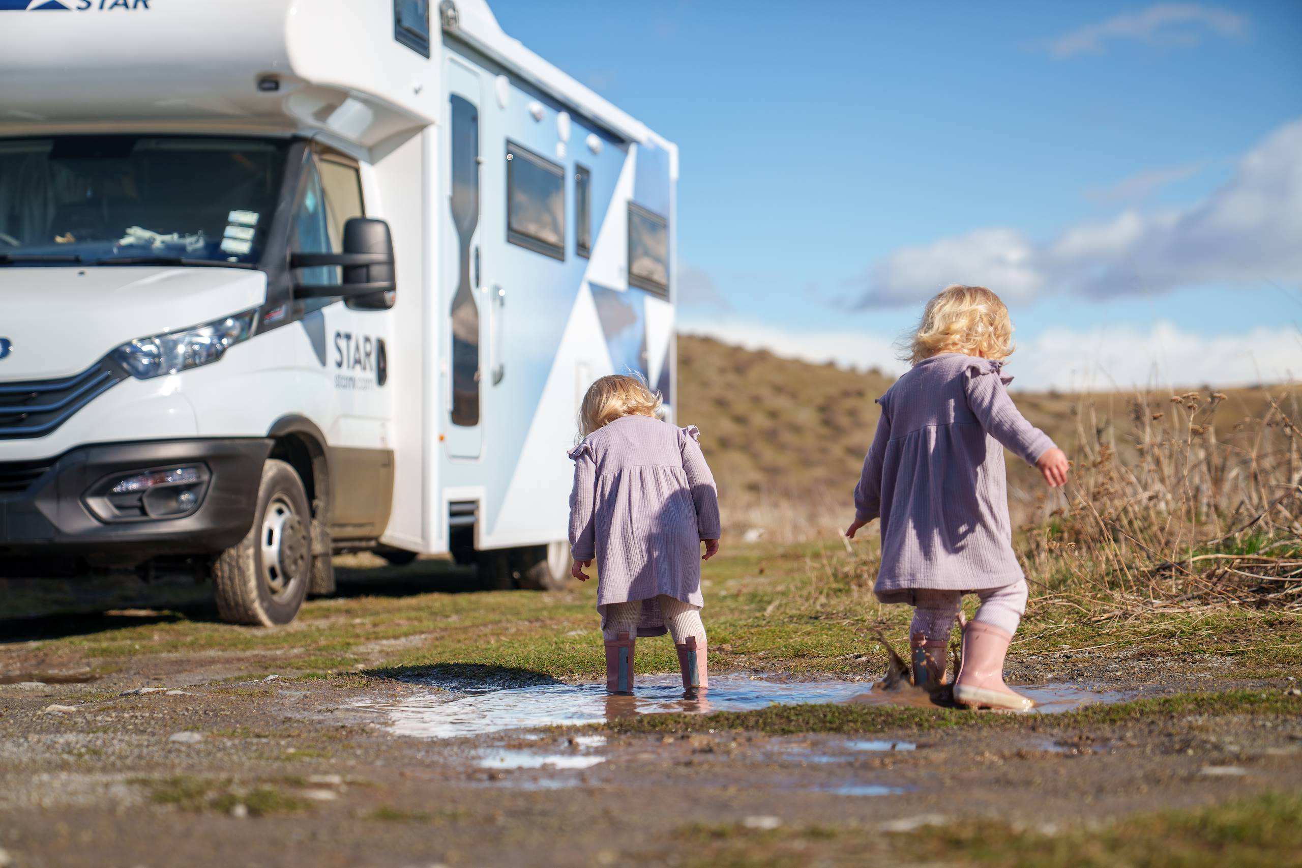 Twin girls jumping in a mud puddle next to Star RV motorhome