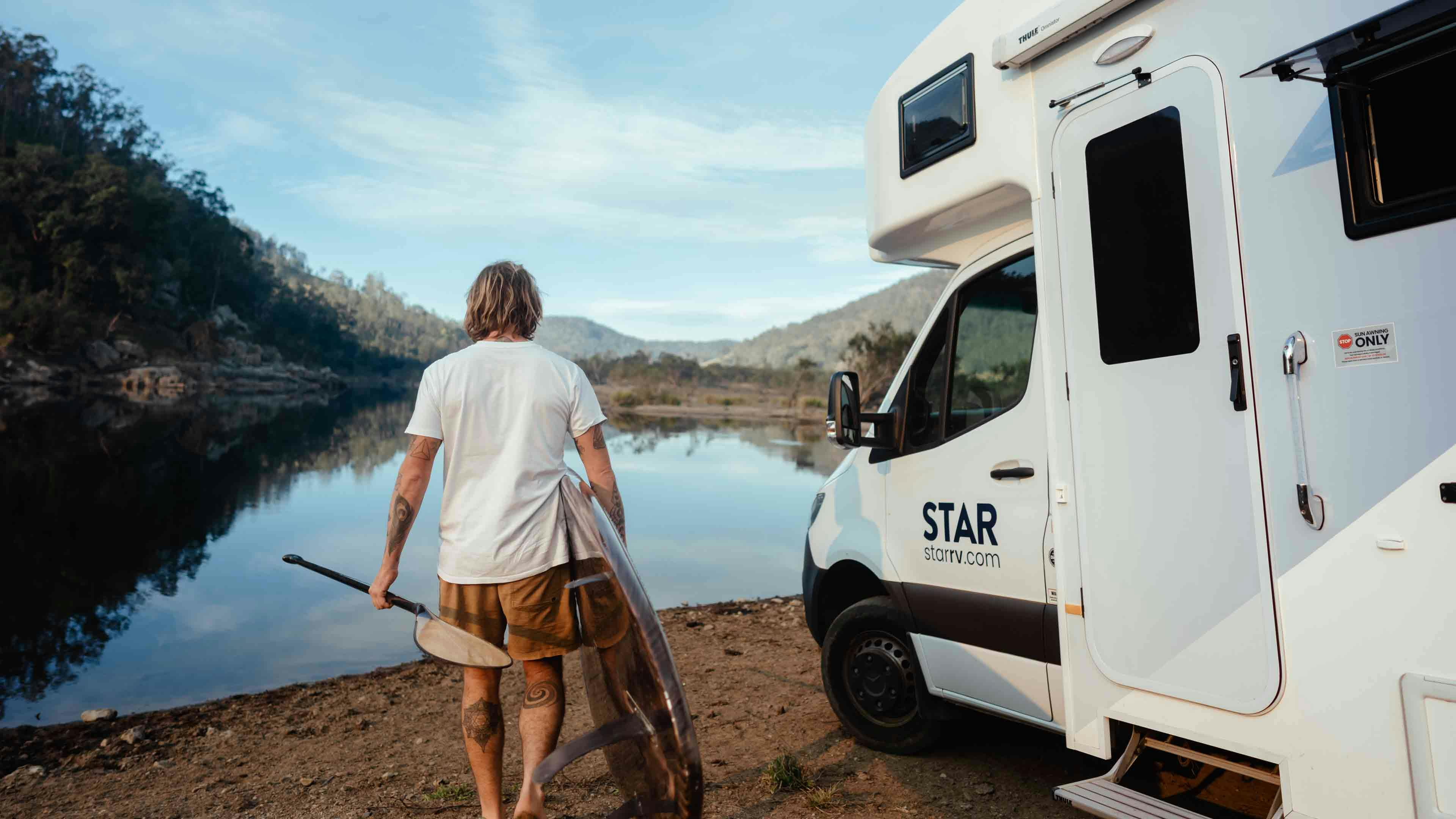 Man with blonde hair with surfboard by Star RV motorhome